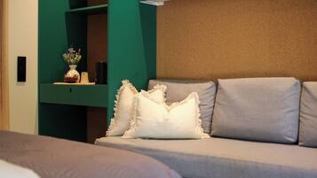 Habitación de hotel moderna con sofá, cojines decorativos, un jarrón con flores y una pared de acento verde.