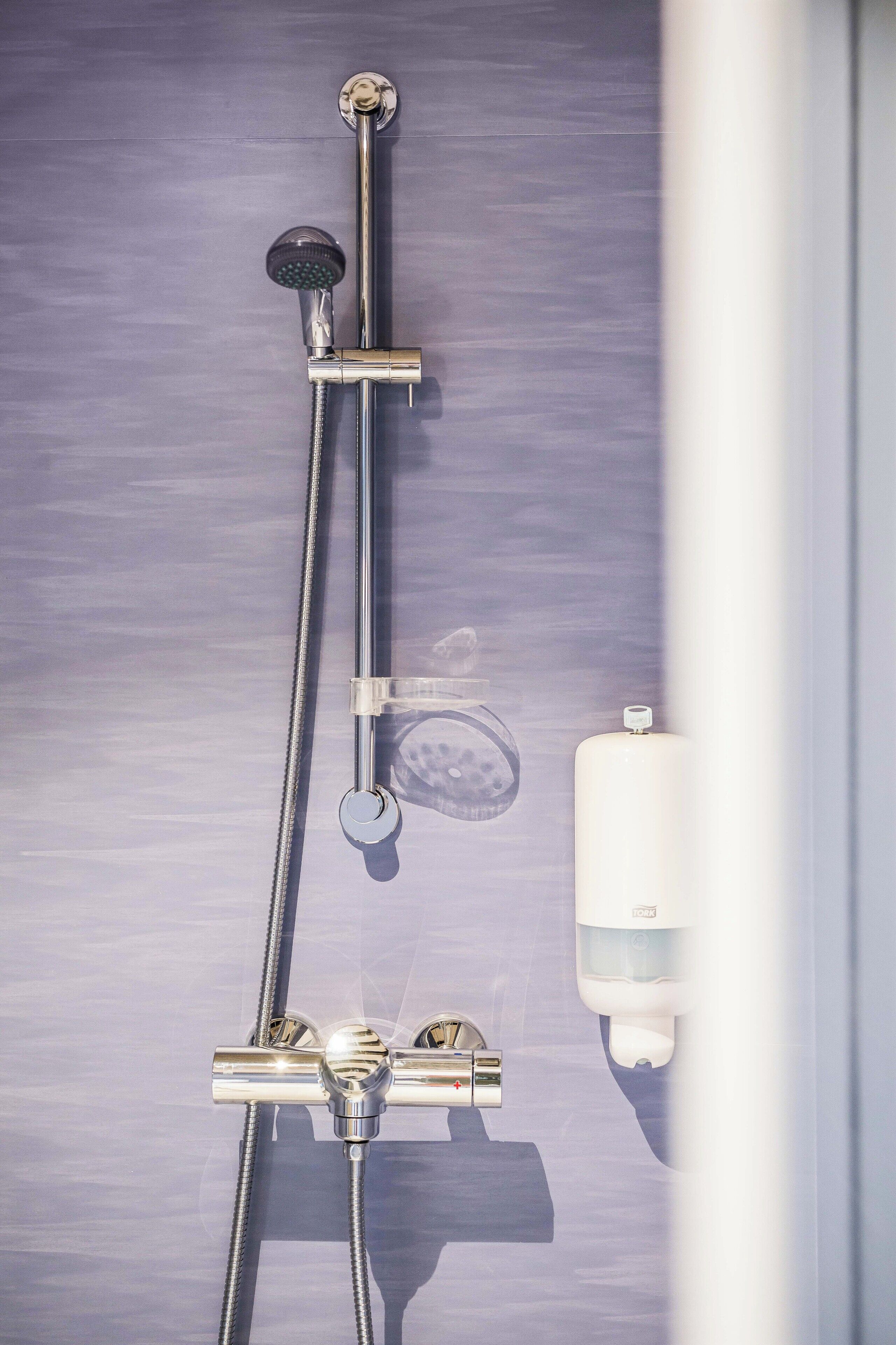 Un baño con ducha, perchero para toallas y dispensador de jabón.