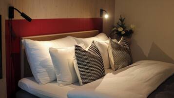 A neatly made bed with white and patterned pillows, a wooden headboard, and a wall-mounted light fixture.