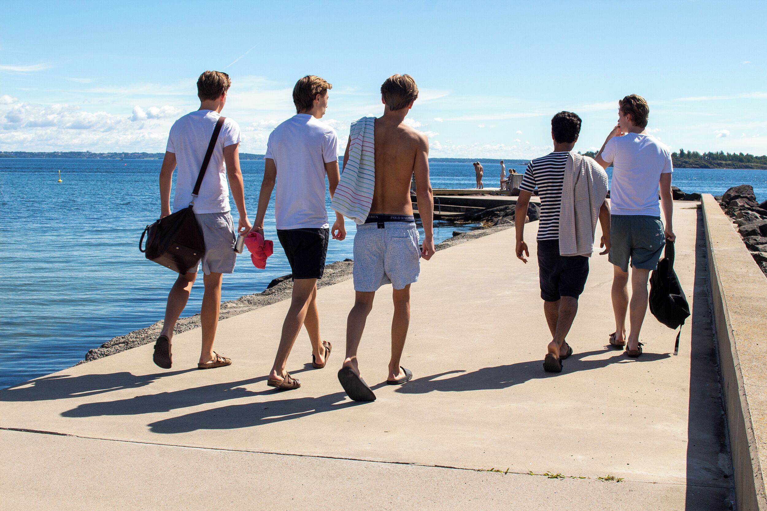 A group of people walking along a concrete path by a body of water.