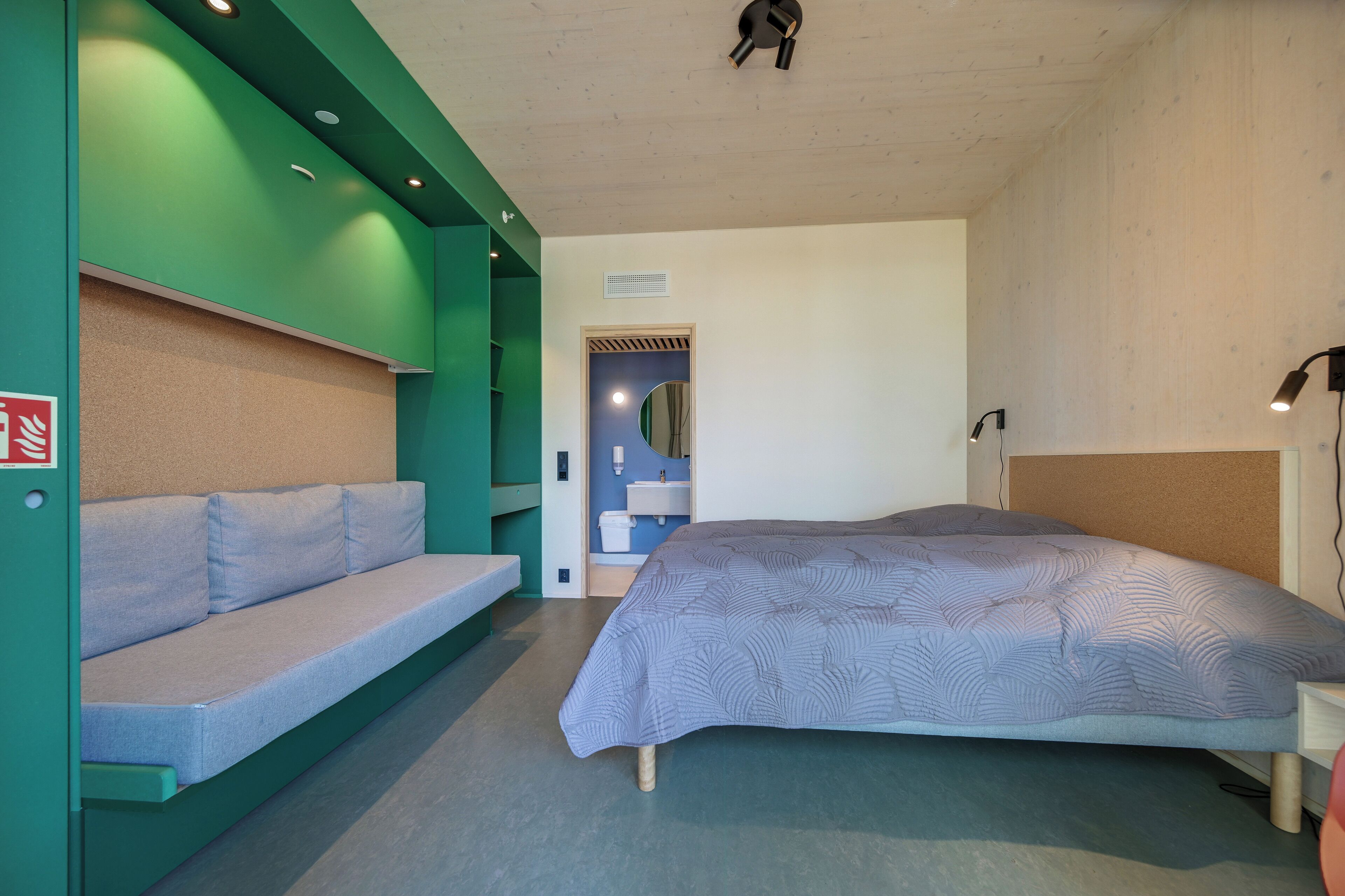 Ein modernes Schlafzimmer mit einem Bett, einer Bank und einem durch eine Tür einsehbaren Badezimmer.