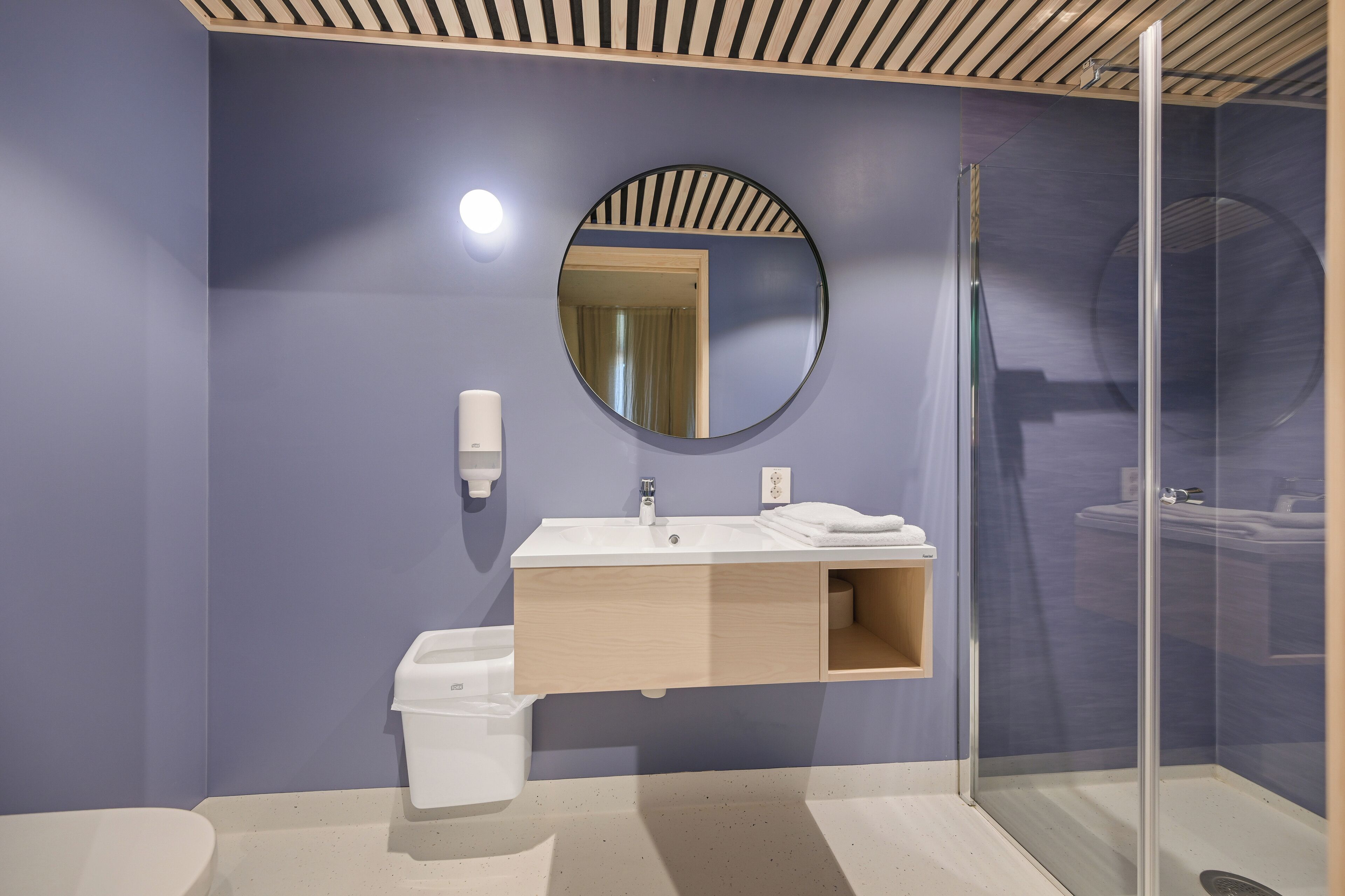 Un baño moderno con tocador de madera, espejo redondo y cabina de ducha de vidrio.