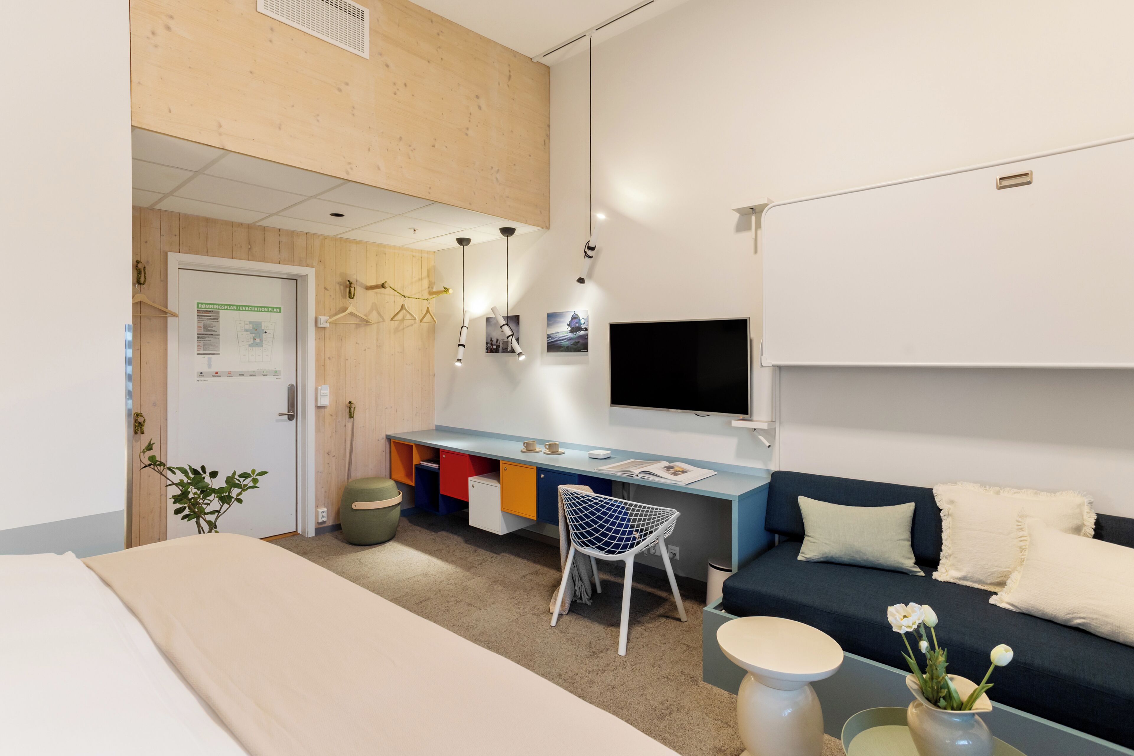 Una habitación moderna con una cama, un escritorio con silla, un sofá, un televisor y una pequeña mesa con un florero.