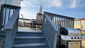 A wooden staircase leading to a deck area with a grill and outdoor furniture.
