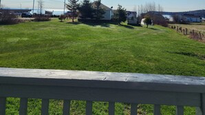 A grassy area with a wooden fence in the foreground, a clear blue sky, and several buildings in the background.