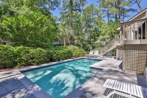 Une piscine dont le bord est revêtu de carrelage, entourée d’une végétation luxuriante et d’arbres.