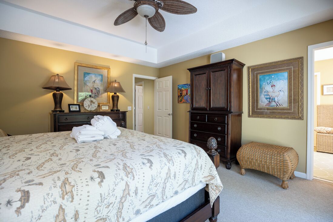 Une chambre à coucher avec un lit, une commode, une lampe et un ventilateur de plafond.