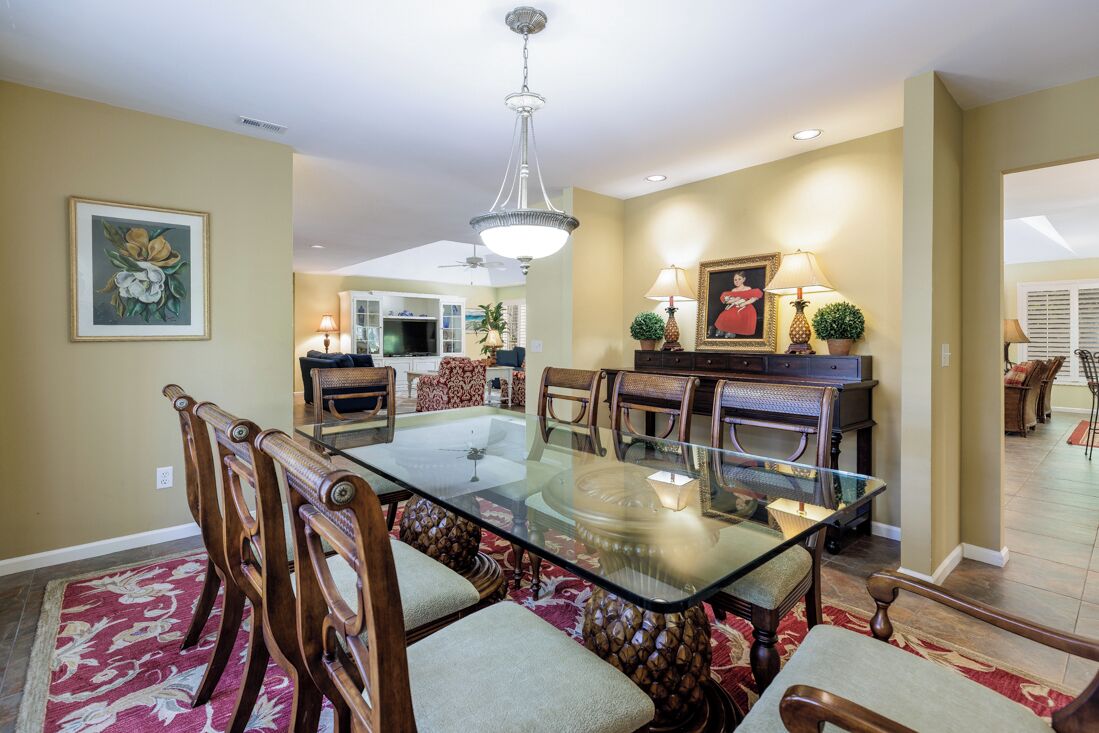 A dining area with a glass-top table, wooden chairs, and a chandelier.