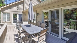Een overdekt terras met een tafel en stoelen, een pergola en een schuifpui die uitkomt op een terras.