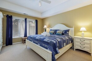 Une chambre à coucher comprenant un lit, des tables de chevet, une fenêtre avec des stores et un ventilateur de plafond.