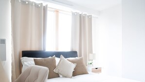 A neatly made bed with white and patterned pillows, a dark headboard, and a bedside table with a lamp and flowers. - The Grand Serenity Suite (London)