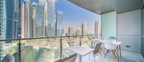 A balcony with a city view, white tables and chairs, and a glass railing.