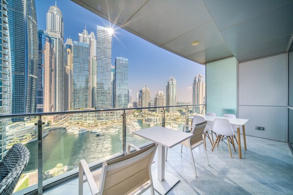 A balcony with a city view, white tables and chairs, and a glass railing.