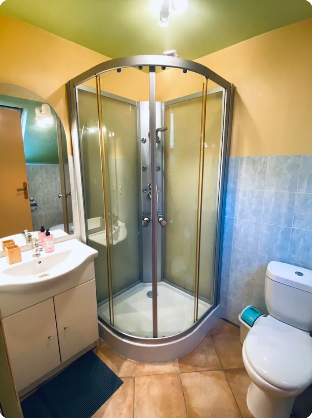 A corner shower with glass doors, a white sink with a mirror, and a toilet.