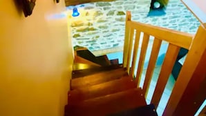 Una scala in legno con corrimano che conduce a una stanza con pavimento in pietra e un lampadario a parete.