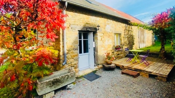 Un cottage in pietra con una porta, un piccolo portico e un giardino con vegetazione colorata.