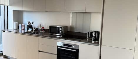 A modern kitchen with white cabinetry, a built-in oven, a microwave, and a coffee maker.