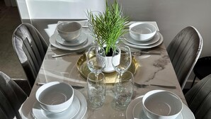 A dining table set with white plates, bowls, and cutlery, centered with a decorative plant and glassware. - Spacious & Luxurious 2-bed Apartment in London (London)