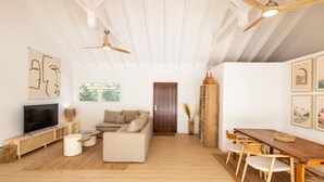 Un grand salon comprenant un canapé, un téléviseur, une table à manger en bois et des ventilateurs de plafond.