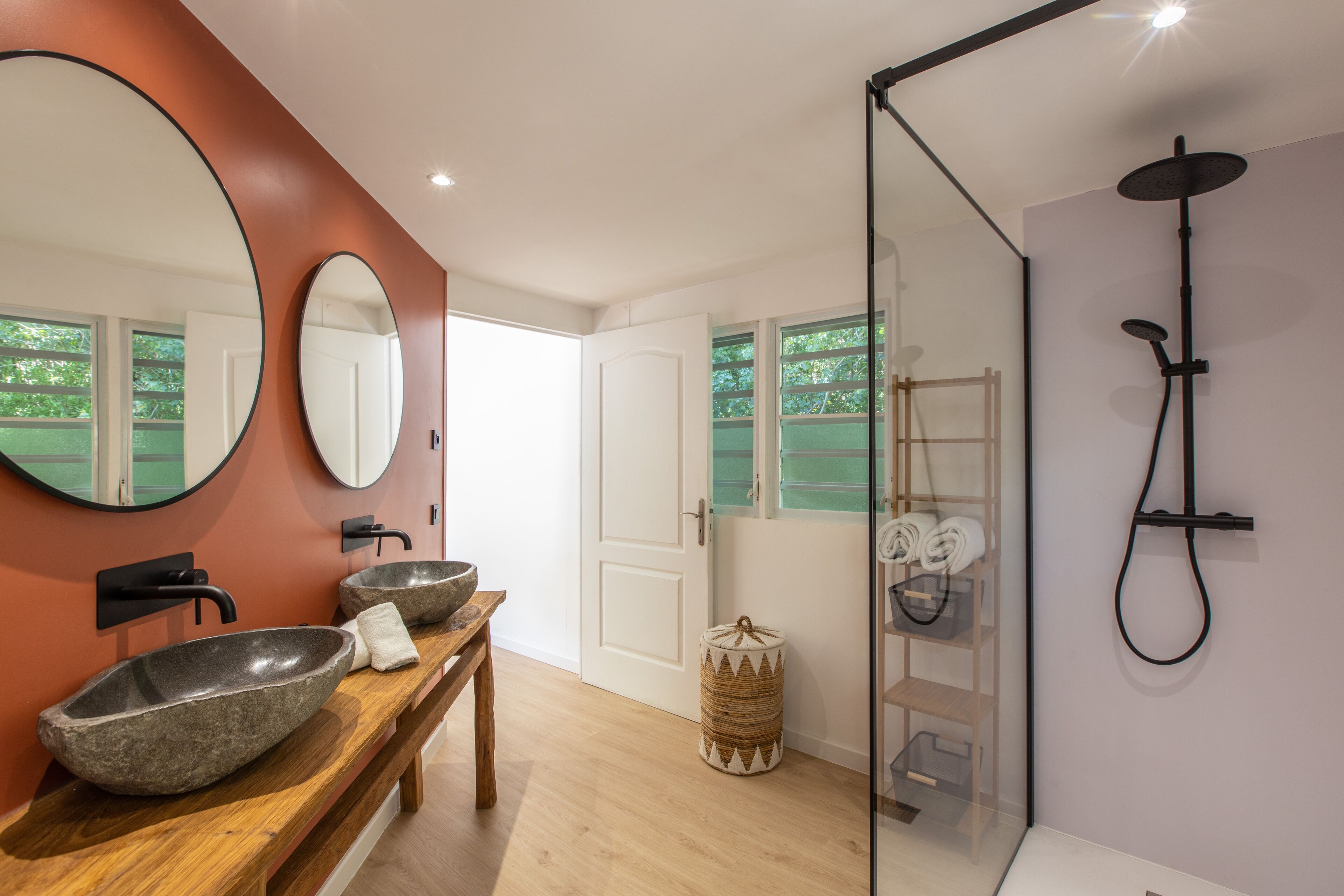 Une salle de bain avec un meuble-lavabo en bois, deux vasques ovales en pierre, un grand miroir, une cabine de douche en verre et un porte-serviettes.