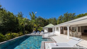 Une piscine avec des chaises longues, un patio couvert et une végétation luxuriante.