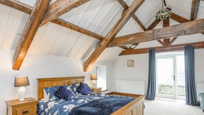 Ein Schlafzimmer mit einem hölzernen Bett, zwei Nachttischen, einer Heizung und Blick ins Freie durch ein großes Fenster.