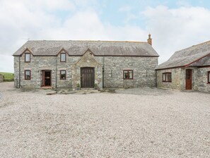 A stone building with a gravel driveway, a wooden door, and multiple windows. - Caerdegog Ganol (Cemaes Bay)