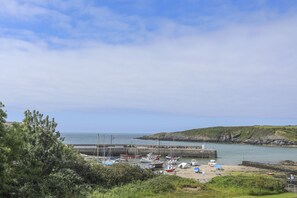 A coastal marina with boats docked, a sandy beach, and a rocky cliff in the background. - Caerdegog Ganol (Cemaes Bay)