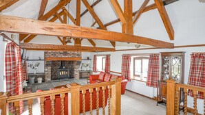Ein geräumiges Wohnzimmer mit freiliegenden Holzbalken, einem Kamin, roten Ledermöbeln und Karottenvorhängen.