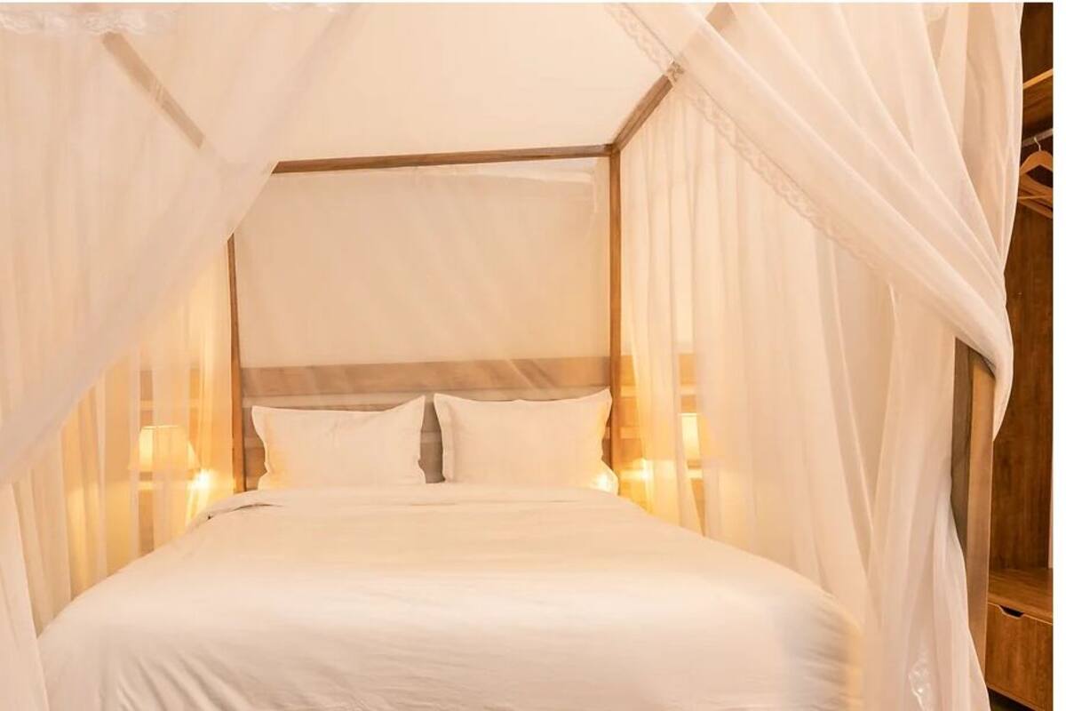 A four-poster canopy bed with white linens and wall-mounted lights.