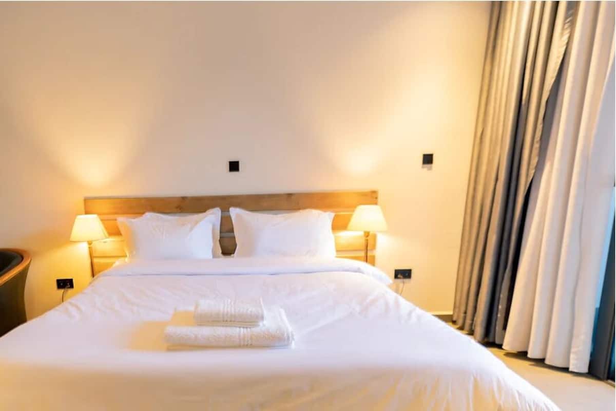 A neatly made bed with white linens, two bedside lamps, a wooden headboard, and a black leather chair.