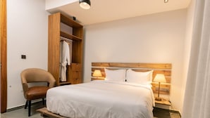 Habitación de hotel con cama de cabecera de madera, armario de madera, una silla y lámparas de noche.