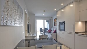 A modern kitchen with white cabinets, a dining area with a glass table, and a living room with a sofa and chairs. - Puerto Feliz 2 : Magnificent renovated penthouse with sea views (Puerto Rico)