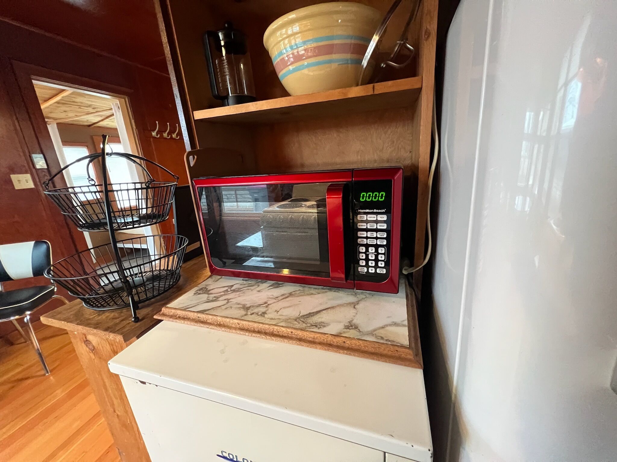 Uma cozinha compacta com um micro-ondas vermelho, uma geladeira branca e uma prateleira de madeira com louças.
