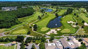 Een golfbaan met een vijver, omgeven door woonwijken en een heldere lucht.
