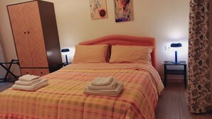 A neatly made bed with a checkered bedspread, two pillows, and folded towels on the side. There are two bedside tables with lamps, a wardrobe, and artwork on the wall. - Apartment for 2 persons with bathroom and equipped kitchen (Salerno)