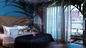 Une chambre d’hôtel moderne avec un grand lit, une petite table avec une bouteille et des verres, et un balcon avec une table et des chaises.