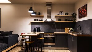 Une cuisine moderne dotée d’un îlot central, d’un four encastré et de meubles en acier inoxydable. On y trouve des tabourets de bar, une machine à café et un luminaire suspendu.