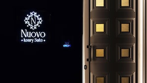 Une porte noire ornée d’un panneau de couleur dorée et d’un panneau lumineux néon indiquant « Nuovo Luxury Suite ».