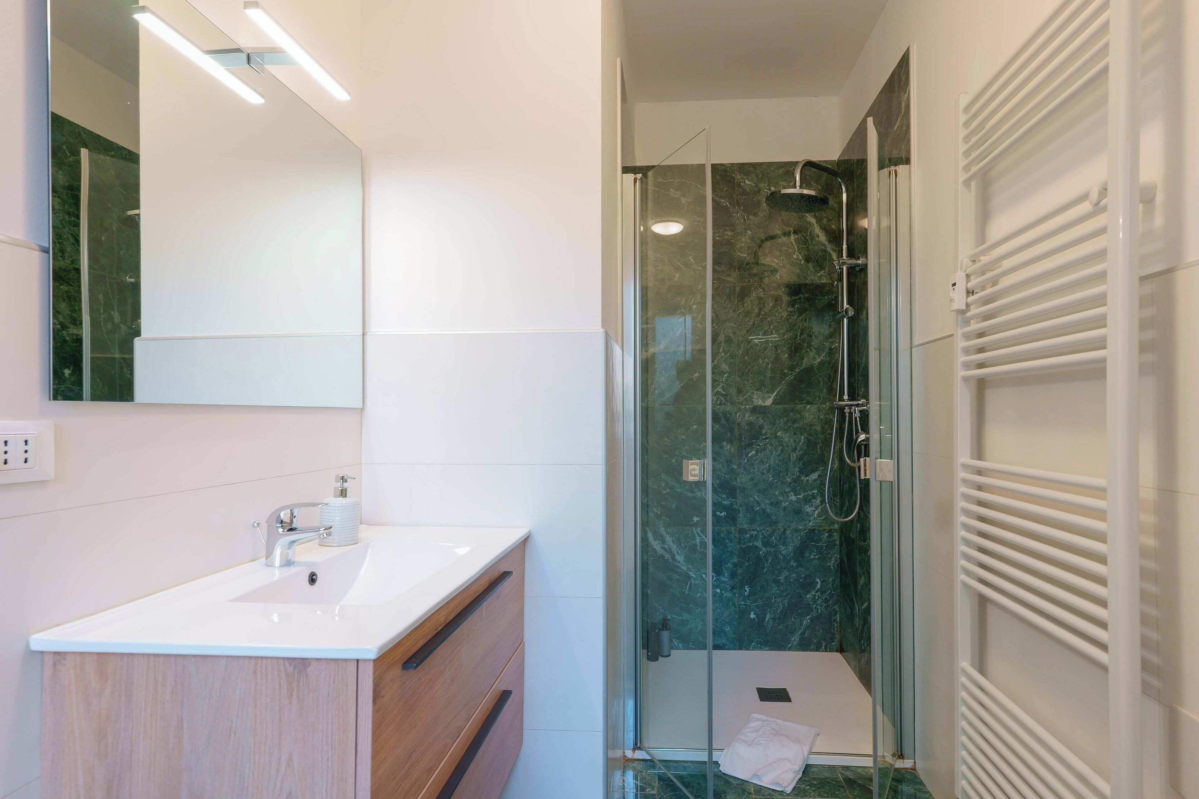Een moderne badkamer met een douchecabine van glas, een witte wastafel en een spiegel.