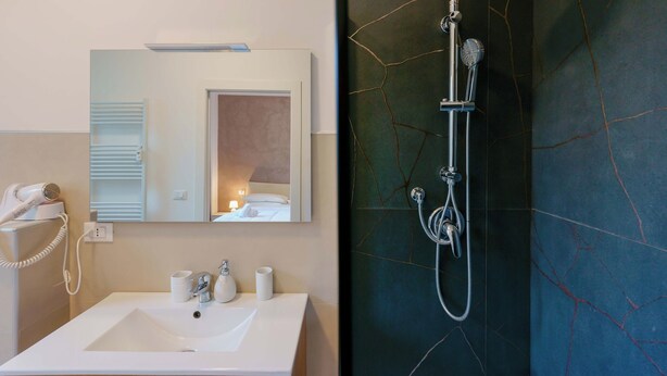A bathroom with a white sink, a mirror, a hairdryer, and a shower with a marble wall. - Le stanze dell'Edera (Bologna)