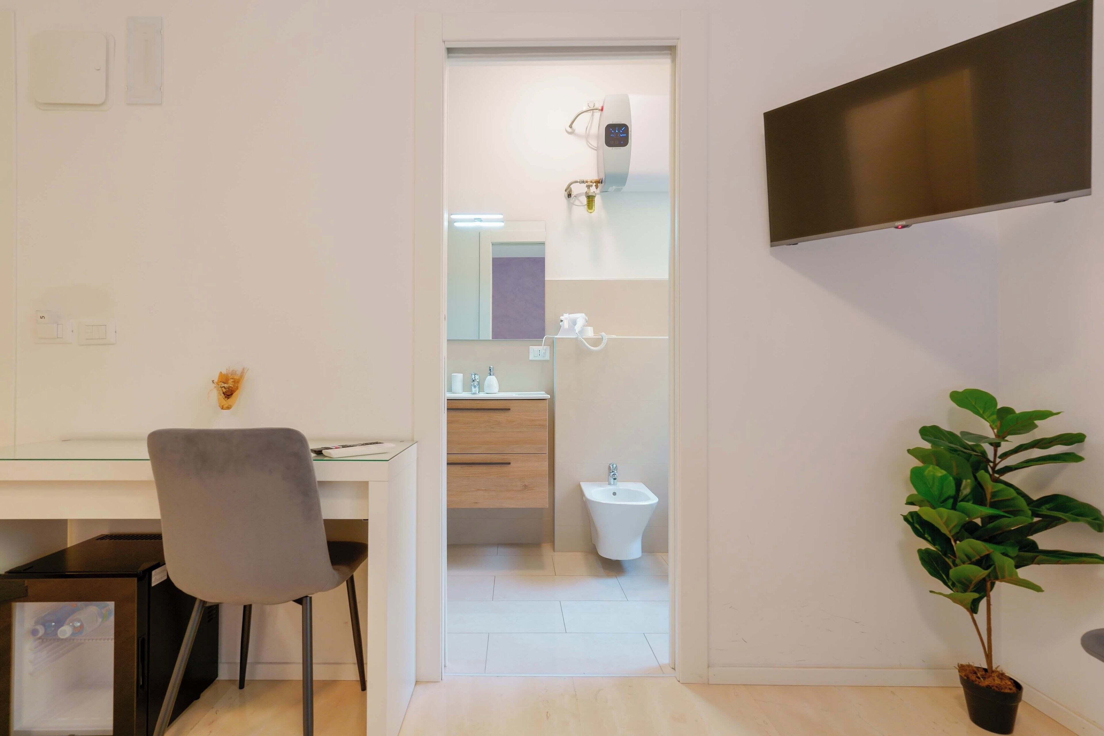 A modern bathroom with a toilet, bidet, and sink. There is a mirror above the sink, and a potted plant is visible.