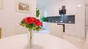 A modern kitchen with white cabinetry, a dining area with a white table, and a vase with red flowers. - Le stanze dell'Edera (Bologna)