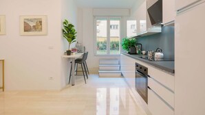 A modern kitchen with a built-in oven, a dining area with a table and chairs, and a large window offering a view of the outside. - Le stanze dell'Edera (Bologna)
