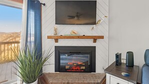 A living room with a fireplace, TV, and a balcony view. - Sea Mist: Oceanfront | Pool and Tennis Access (Nags Head)