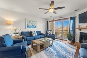 A living room with a ceiling fan, a sofa set, a coffee table, a fireplace, and a large window with a view.