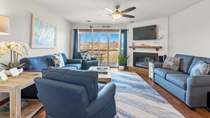 A modern living room with a blue sofa, a coffee table, a TV, and a fireplace. - Sea Mist: Oceanfront | Pool and Tennis Access (Nags Head)