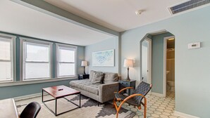 A living room with a sofa, two chairs, a coffee table, and a lamp. There is a window with blinds, a door leading to a bathroom, and a tiled floor. - 🐚 Seaside Cottage A: Pet-Friendly Cottage, Steps to the Beach! 🐚 (Carolina Beach)