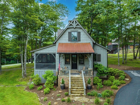 A small, single-story house with a front porch, a stone staircase, and a well-maintained garden.