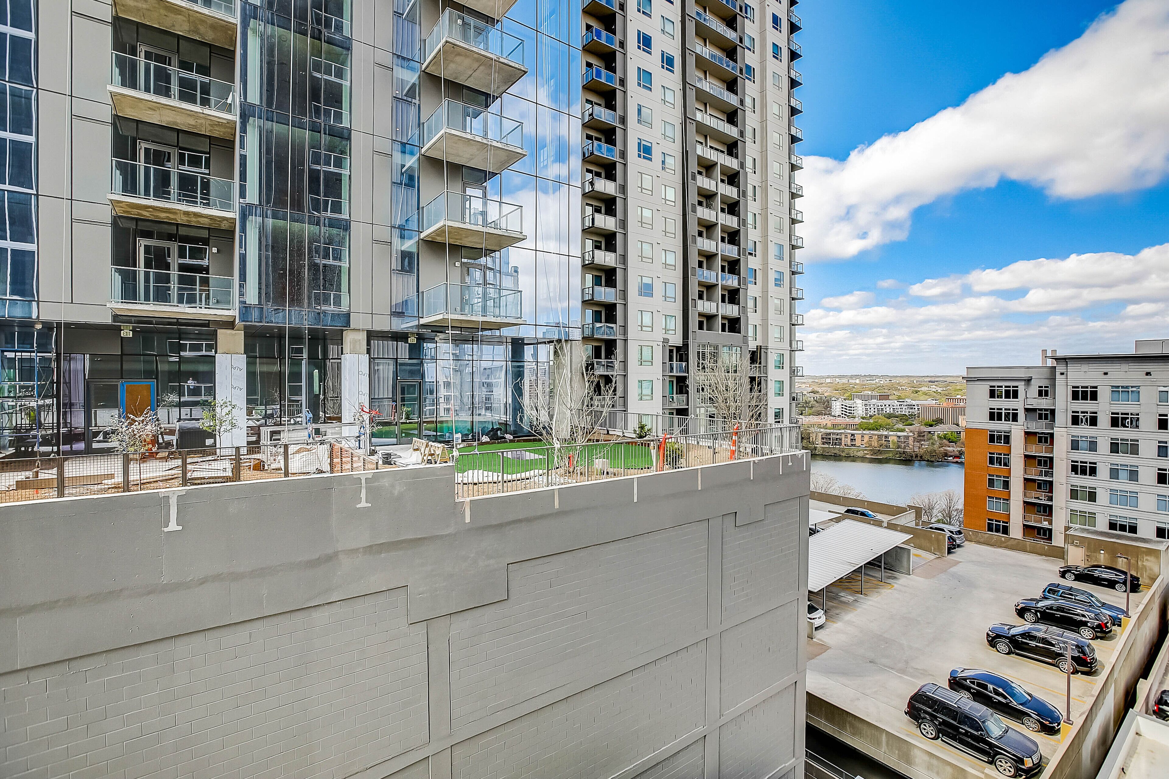 A high-rise building with multiple balconies, a parking area, and a view of a river.